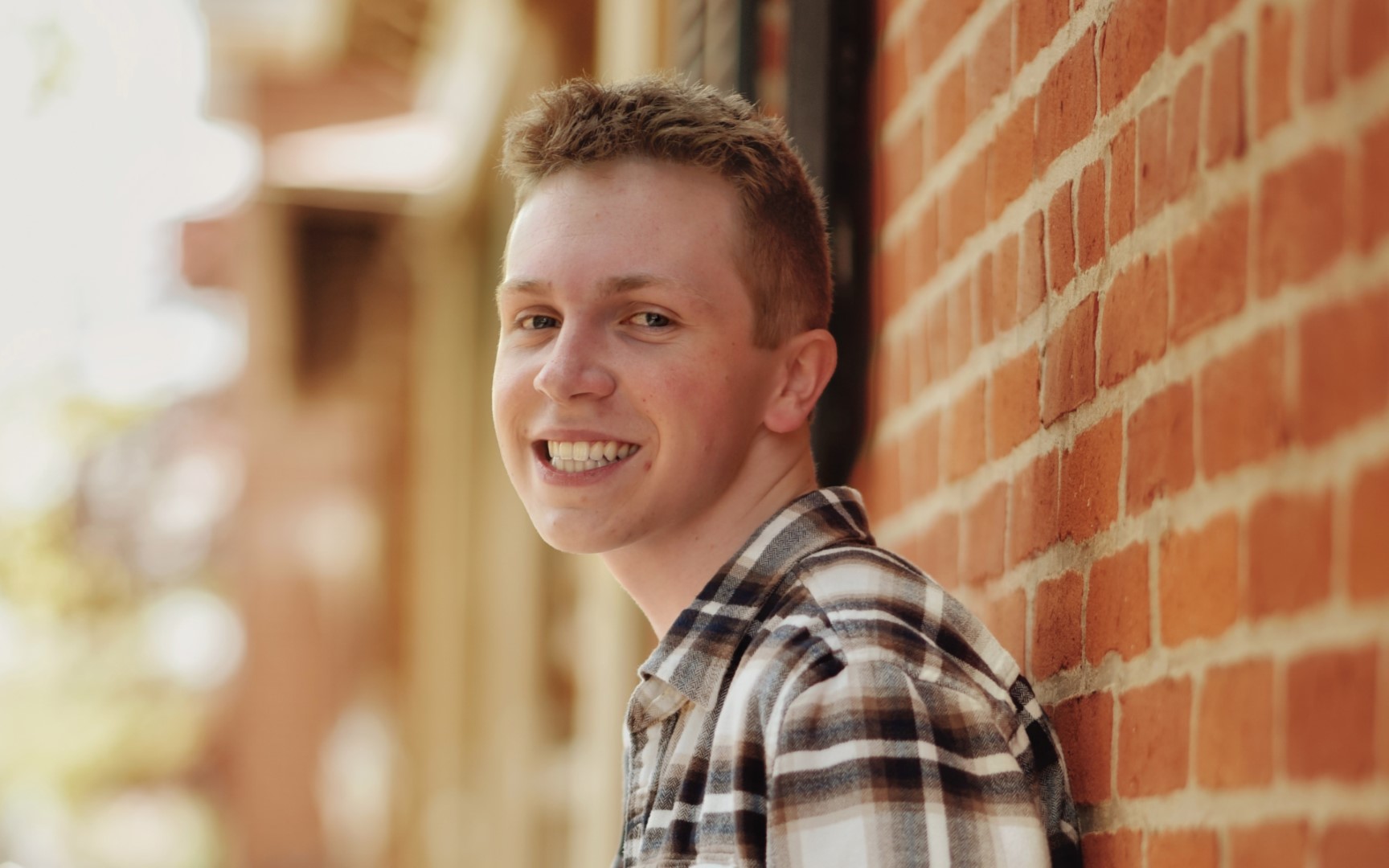 young man smiles while leaning against a brick wall