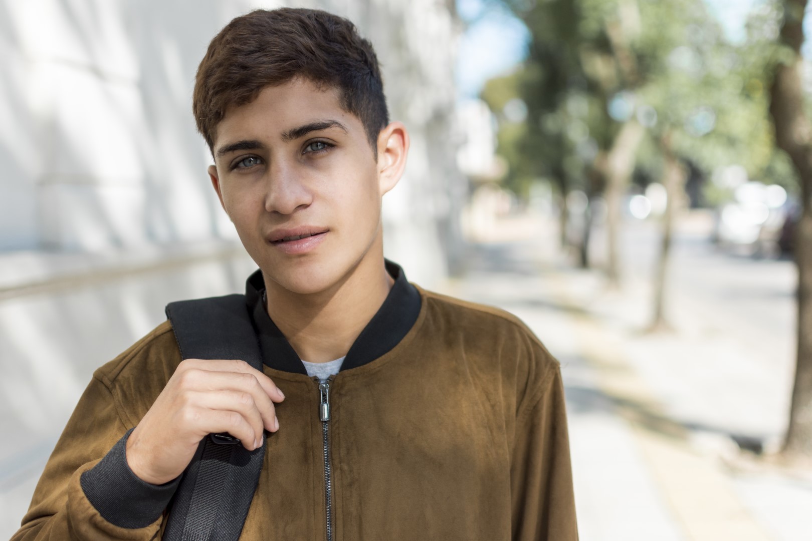 Dark haired teenage boy standing outside on an sunny street