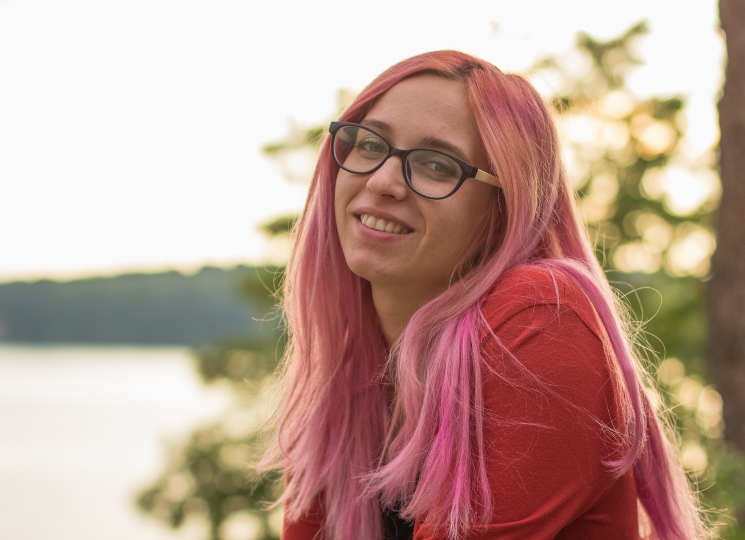 teenage girl with pink hair sits outside in the sun